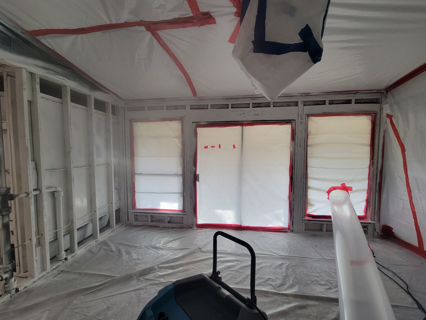 A residential room sealed with plastic sheeting covering windows, walls, and floor..